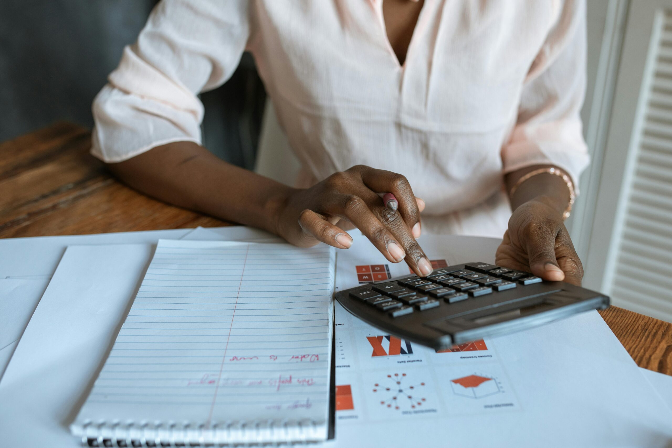 A professional woman calculating finances at a desk with charts and a calculator.